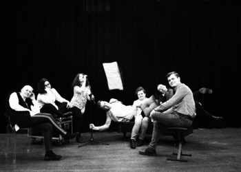 Czarno-białe zdjęcie przedstawiające 7 osób, które przyjmują różne pozycje na scenie.