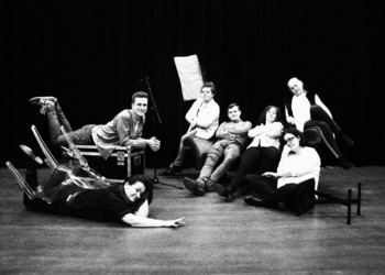 Czarno-białe zdjęcie przedstawiające 7 osób, które w różnych pozycjach siedzą lub leżą na scenie.